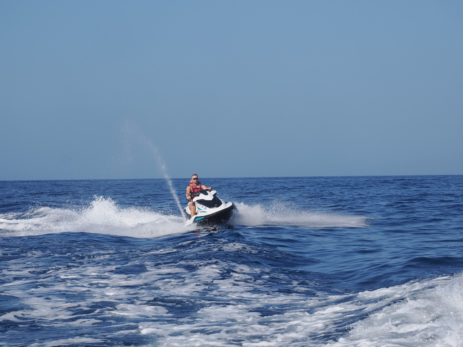 Rider leaning a jet ski into a turn, throwing spray on blue Atlantic water